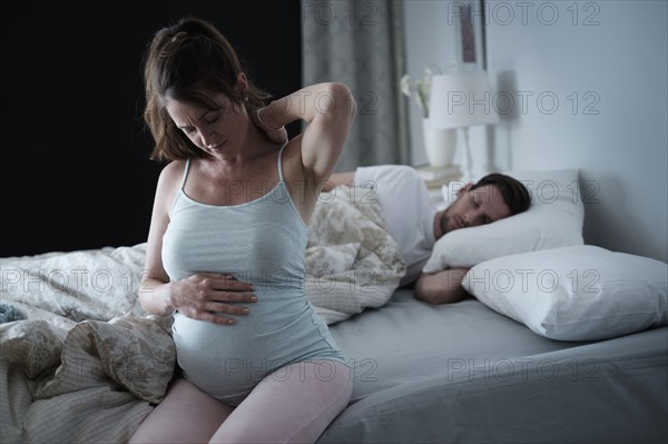 Woman sitting on bed and stretching stiff neck.