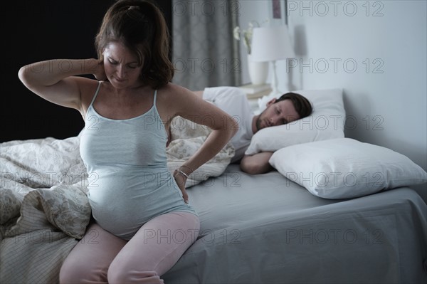 Woman sitting on bed and stretching stiff neck.