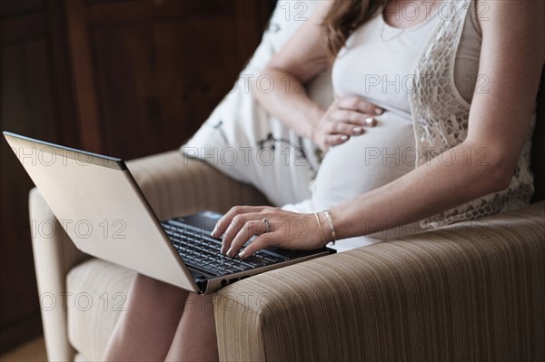 Mid-section of pregnant woman using laptop.