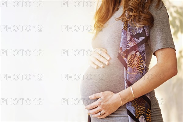 Mid-section of pregnant woman outdoors.