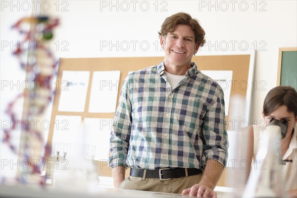 Portrait of teacher indoors, girl (10-11) using microscope in background.