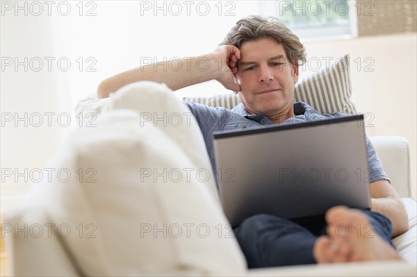 Mature man using laptop on sofa.