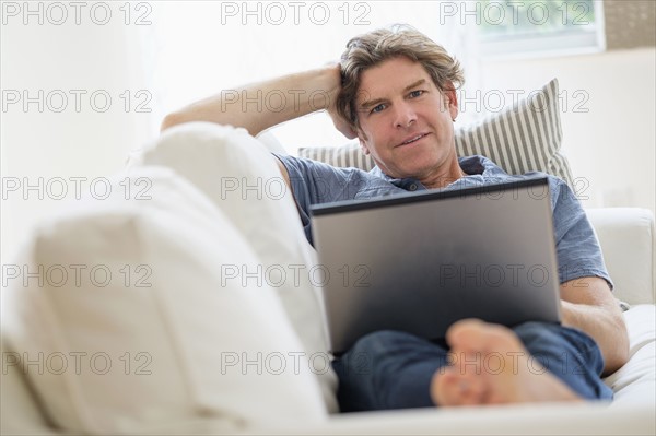 Mature man using laptop on sofa.