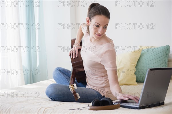 Woman with laptop and guitar on bed