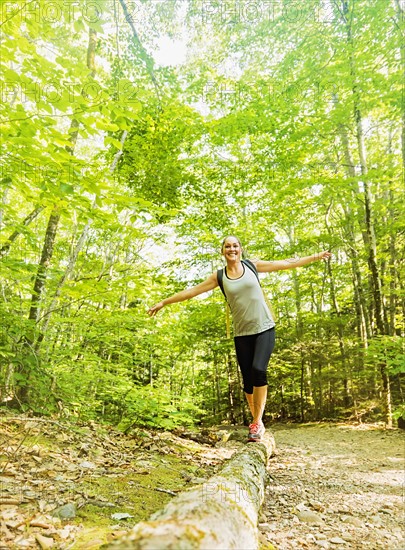 Female hiker walking along log in forest