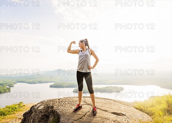 Young woman standing on top of mountain and flexing muscles