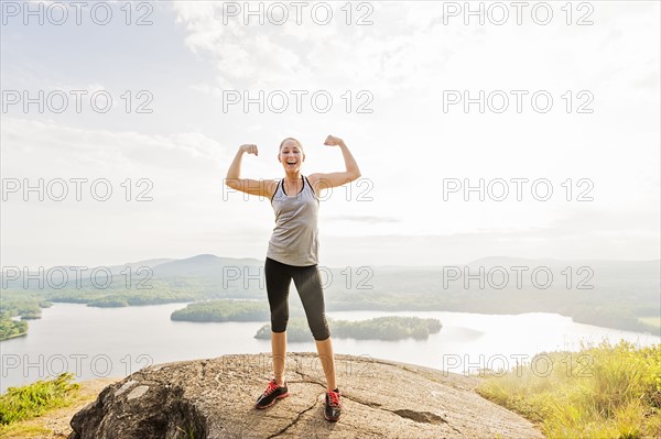 Young woman standing on top of mountain and flexing muscles