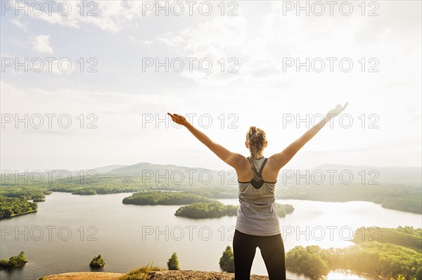 Young woman standing on top of mountain with outstretched arms, rear view