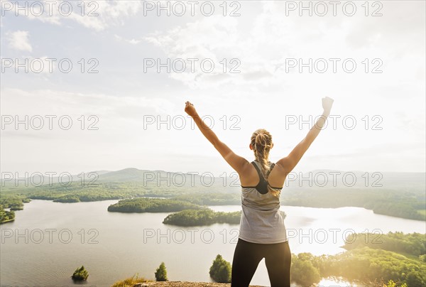 Young woman standing on top of mountain with outstretched arms, rear view