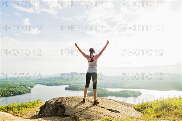 Young woman standing on top of mountain with outstretched arms, rear view