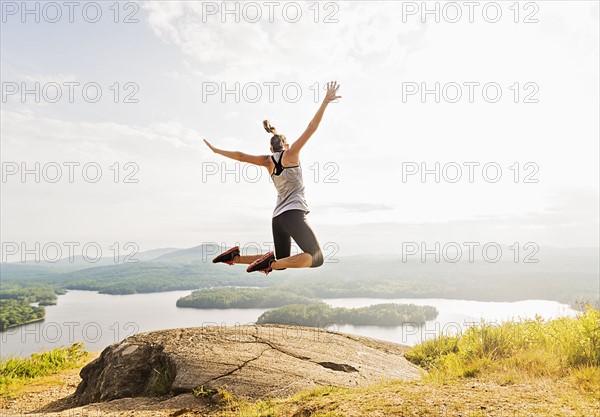 Young woman jumping over mountain top, rear view