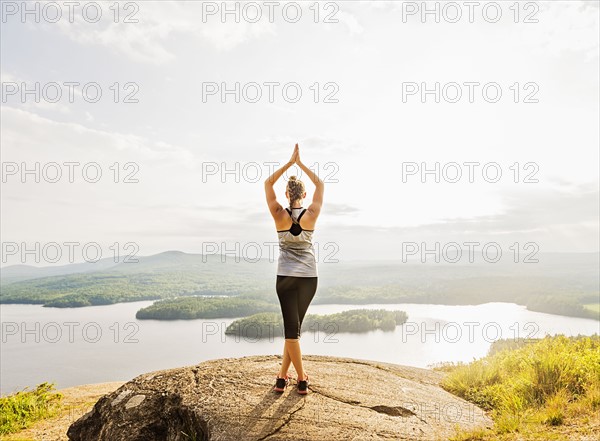 Rear view of young woman practicing yoga in front of lake