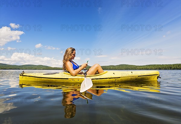 Young woman using Smartphone in kayak on lake