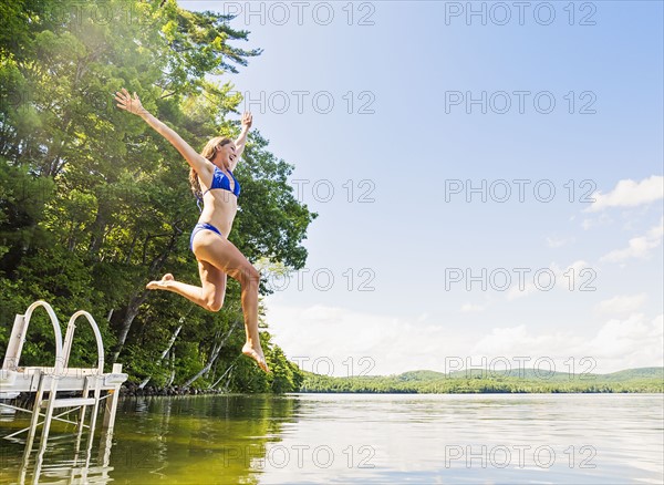 Young woman jumping into lake from jetty