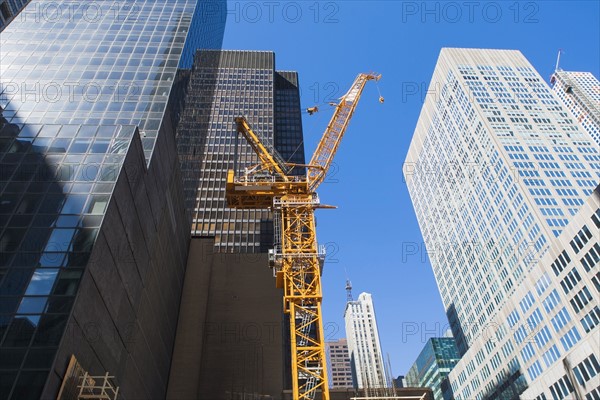 Low angle view of crane among skyscrapers