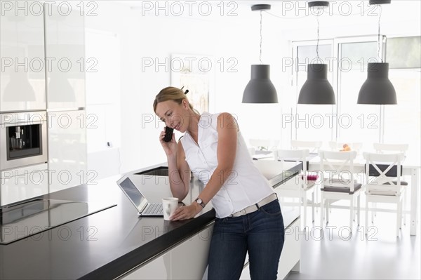 Woman with laptop in kitchen talking on phone