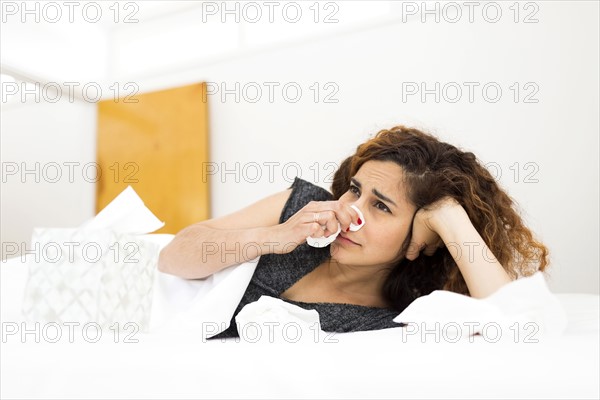 Woman blowing nose in bed