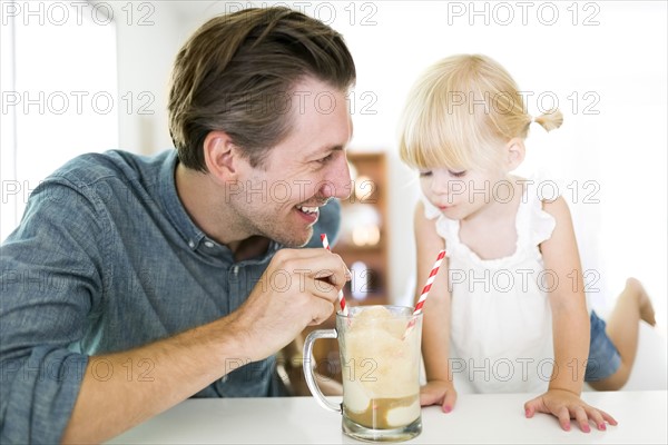 Father drinking milkshake with daughter (2-3)