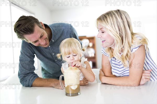 Girl (2-3) drinking milkshake with parents at home