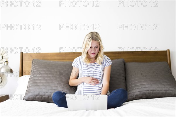 Pregnant woman using laptop in bed