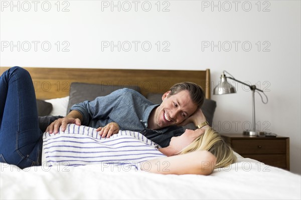 Husband lying down on bed with pregnant wife