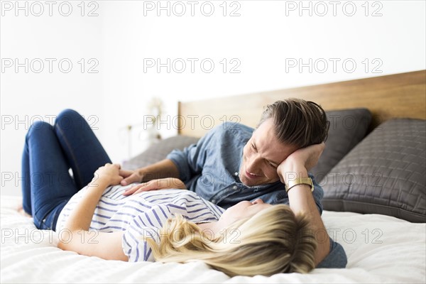 Husband lying down on bed with pregnant wife