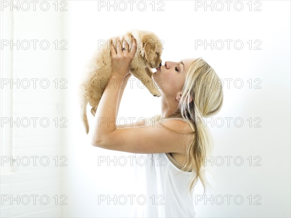 Studio shot of owner kissing Golden Retriever puppy