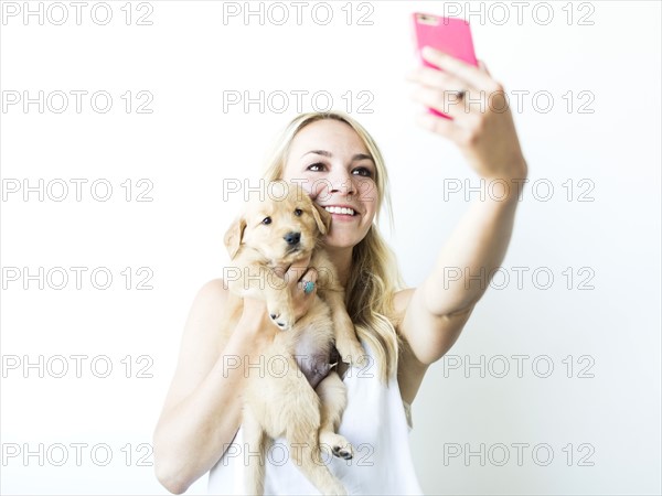 Studio shot of woman photographing self with Golden Retriever puppy