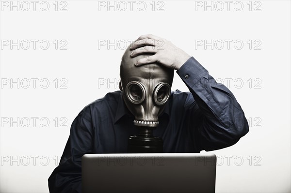 Studio shot of man in front of laptop wearing gas mask