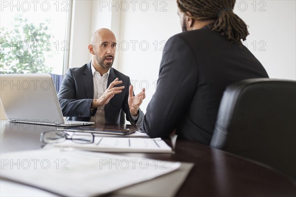 Two businessmen having discussion at desk in office.