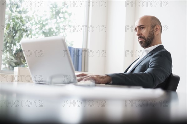 Concentrated businessman working with laptop at desk in office.