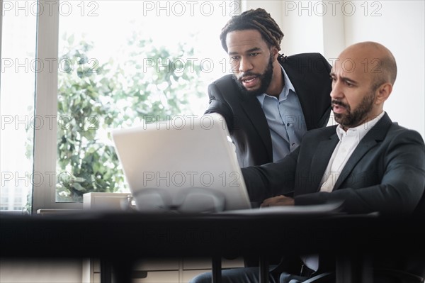 Two businessmen working with laptop by desk in office.