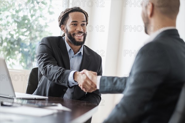 Smiling businessmen shaking hands in office.