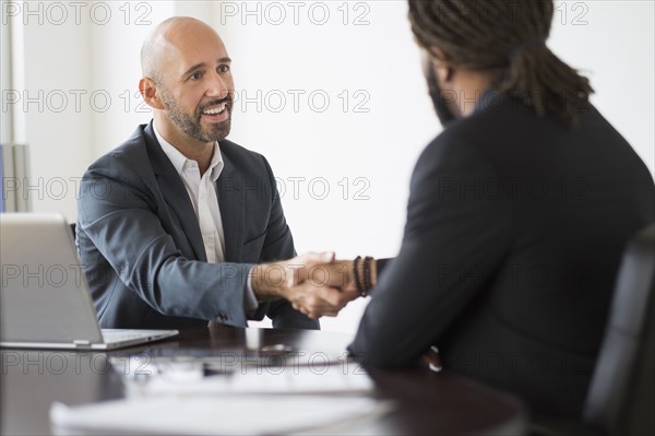 Smiling businessmen shaking hands in office.