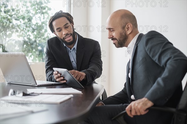 Two businessmen working with digital tablet by desk in office.