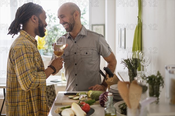 Smiley homosexual couple drinking wine in kitchen.