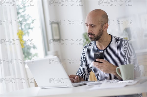 Man working with laptop and holding smart phone at table.