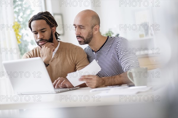 Two men working with laptop at table at home.