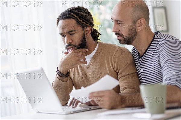 Two men working with laptop at table at home.