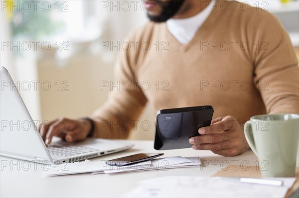 Man working with laptop at table and holding digital tablet.