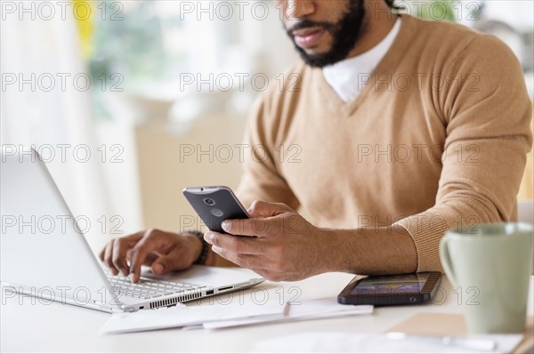 Man working with laptop at table and holding smart phone.