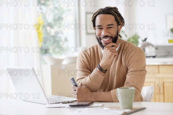Portrait of smiley young man with laptop at table.