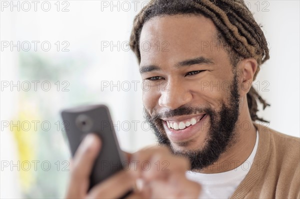 Smiley young man with dreadlocks using smart phone.