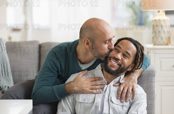 Homosexual couple kissing by sofa in living room.