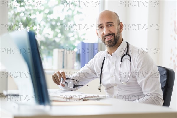 Portrait of smiley doctor working with laptop at desk in office.