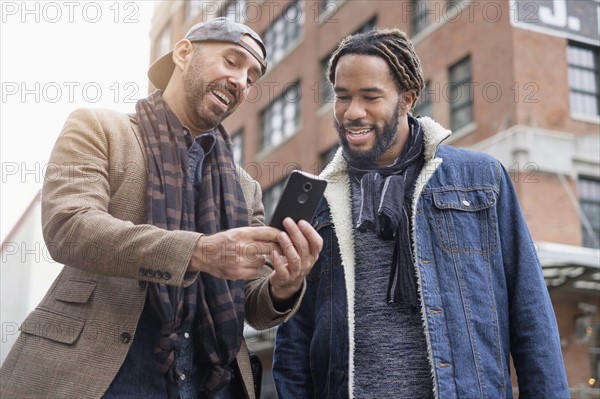 Smiley homosexual couple taking selfie with smart phone in street.