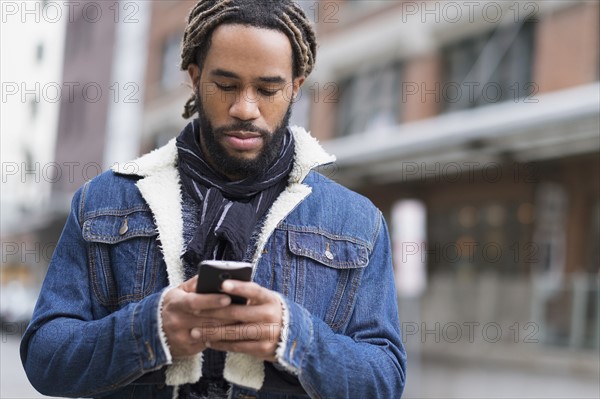 Serious man with dreadlocks using smart phone in street.