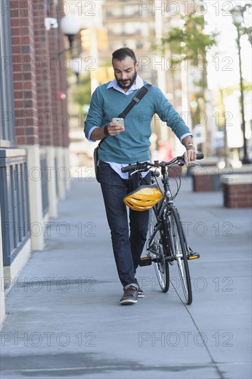 Man walking with bicycle using phone.