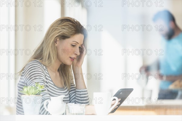 Young woman using tablet and man in background.