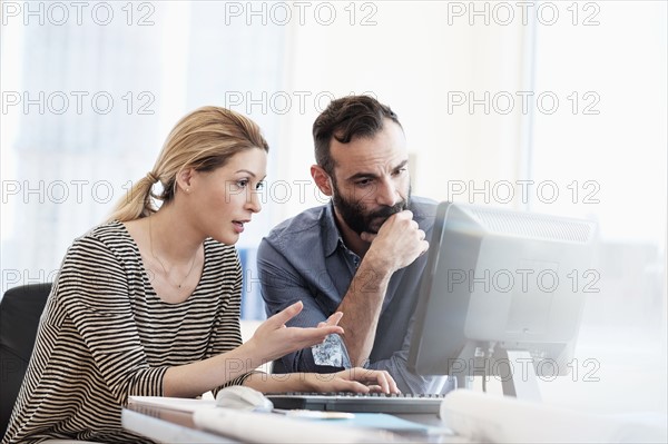 Man and woman looking at computer in office.